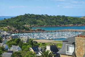 A coastal town with a marina, houses, and a forested hill. - Appartement avec vue mer, bercé par les embruns (TREBEURDEN)