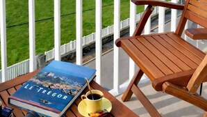 Ein Holztisch und ein Stuhl auf einem Balkon mit einem Buch, einer Tasse und einem Fernglas.