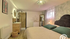 Ein Schlafzimmer mit Bett, Kommode, Spiegel und Duschbereich.