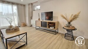 Ein modernes Wohnzimmer mit Holzboden, einem Fernseher auf einem Holzbodenständer, einem Esstisch und einer Zimmerpflanze.