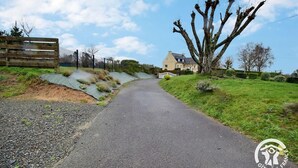 Eine Landstraße führt zu einem Haus mit eingezäuntem Garten und einem großen Baum.