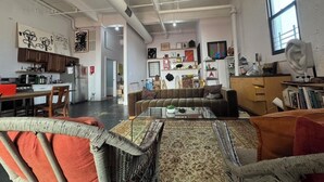 A spacious living area with a sofa, a glass coffee table, and a dining table with chairs. There is a kitchen area visible in the background.