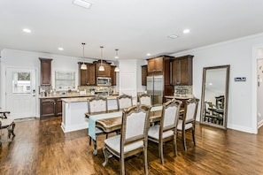 A spacious kitchen with wooden cabinets, a central island, and a dining area with a large table and chairs. - The Sandy Feet Retreat - Private Backyard Oasis With Swimming Pool - Just Minutes From Navarre Beach (Navarre)