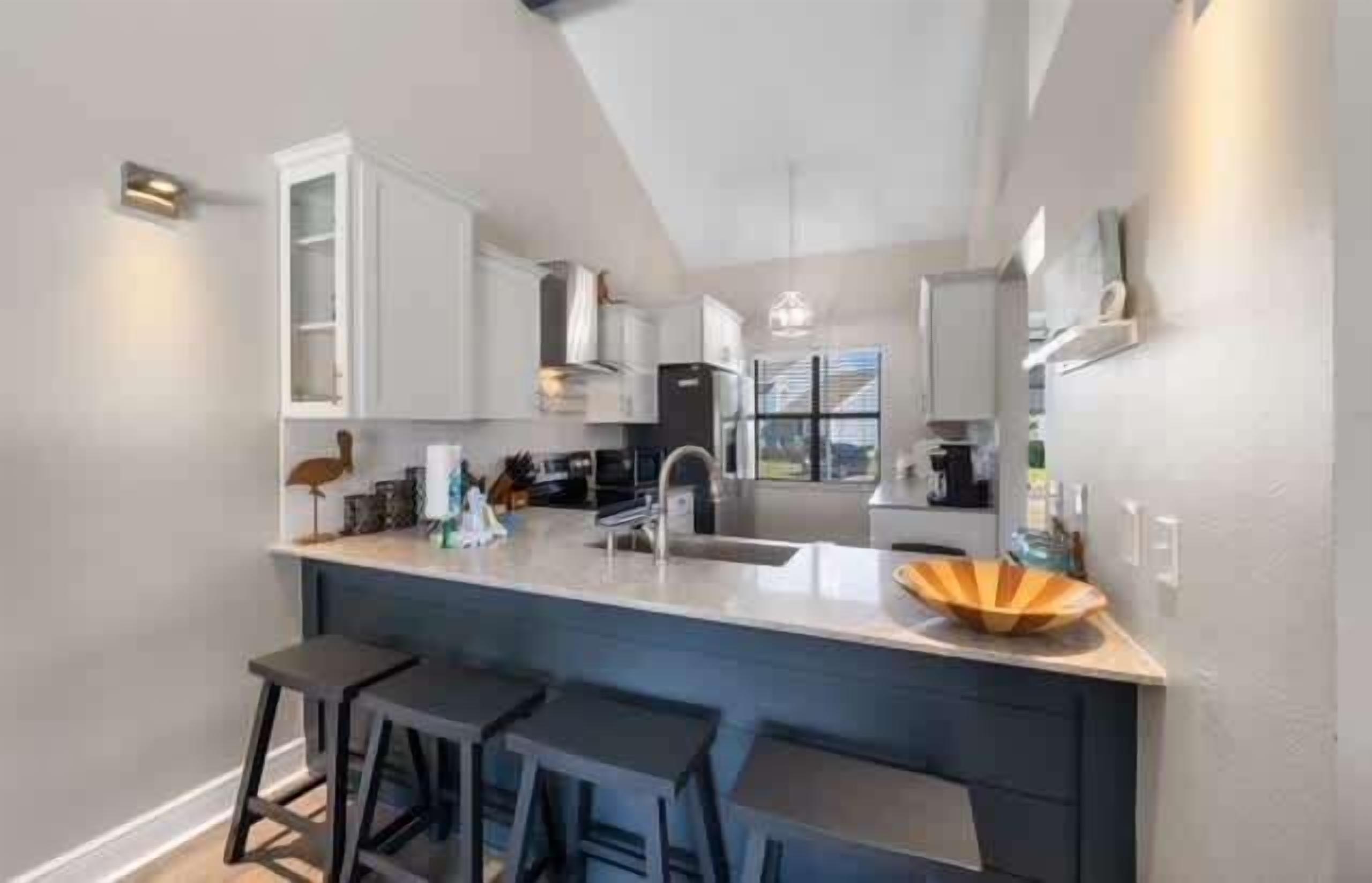 A modern kitchen with white cabinets, a central island with stools, and a large window.