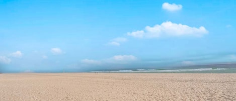 A wide sandy beach with a clear blue sky and a few clouds.