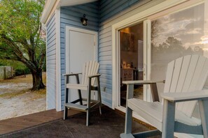 A porch with two Adirondack chairs, a wooden deck, and a door leading to a covered area with a window. - Sandy Toes Retreat @ Mariner Lakes – Beautiful Condo with Easy Beach Access! (Orange Beach)