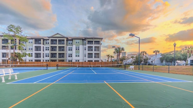 Una cancha de tenis al aire libre con una valla de madera, rodeada de edificios de varios pisos con balcones.