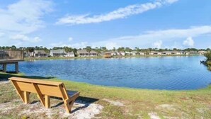 Vista a un lago con un banco de madera, un muelle y una hilera de casas a orillas del agua.