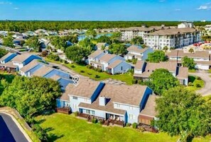 A residential area with multiple houses, a large building, and a body of water in the background. - Sandy Toes Retreat @ Mariner Lakes – Beautiful Condo with Easy Beach Access! (Orange Beach)