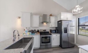 A modern kitchen with white cabinets, a stainless steel refrigerator, a microwave, and an oven. - Sandy Toes Retreat @ Mariner Lakes – Beautiful Condo with Easy Beach Access! (Orange Beach)