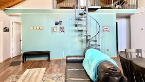 Un loft spacieux avec un plafond haut, un escalier en colimaçon, un canapé en cuir et un coin repas.