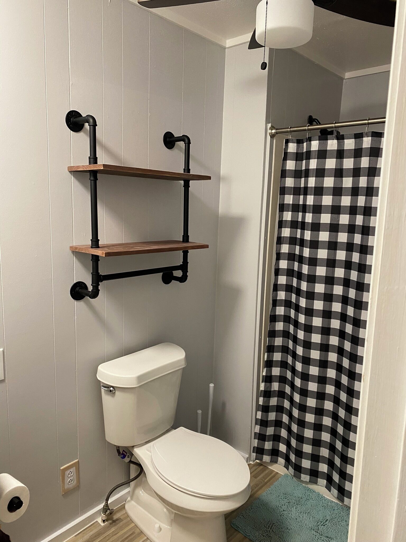 A bathroom with a white toilet, a black and white checkered shower curtain, and wooden shelves mounted on the wall.