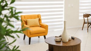Een kamer met een gele fauteuil, een witte vaas en een houten bijzettafeltje.