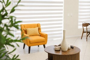 Ein Zimmer mit einem gelben Sessel, einer weißen Vase und einem Holztisch.