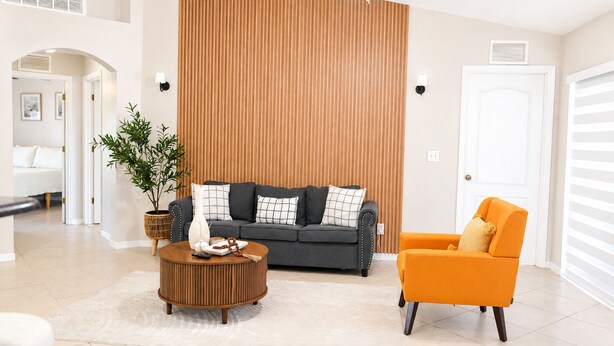 Een moderne woonkamer met een grijze bank, een oranje fauteuil, een houten accentmuur en een potplant.