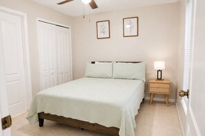 Ein Schlafzimmer mit einem Bett, einem Nachttisch, einem Deckenventilator und zwei gerahmten Bildern an der Wand.