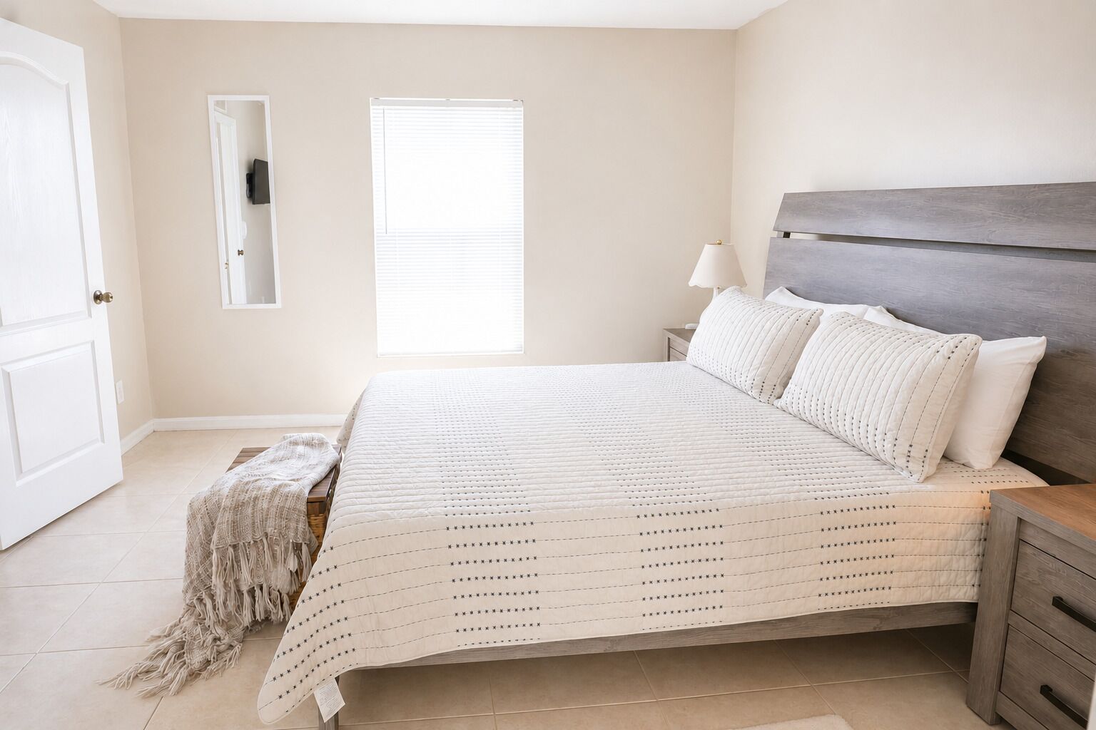 Une chambre à coucher avec un lit, des tables de chevet, un miroir et une fenêtre.