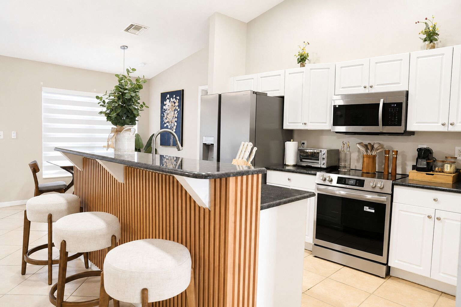 A modern kitchen with white cabinets, a central island with stools, stainless steel appliances, and a potted plant.