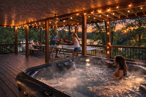 A hot tub with people around it, a wooden deck, and string lights. - Luxury Lakefront | Kayaks, Creek, Hot tub, & Views (Ellijay)