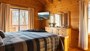 Een houten slaapkamer met een bed, een kapstok en een televisie aan de muur.
