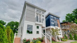Ein zweistöckiges Wohngebäude mit weißer Fassade, einem Balkon im oberen Geschoss und einer Treppe zum Eingang.