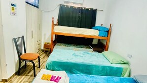 Una habitación pequeña y limpia con una cama doble, un escritorio con silla y un televisor en la pared.