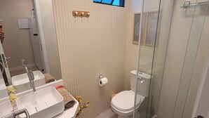 A modern bathroom with a large mirror, dual sinks, a toilet, and a glass-enclosed shower. - Paradise in Praça 19: 3 min from the village and 5 min from the natural pools! (Ipojuca)
