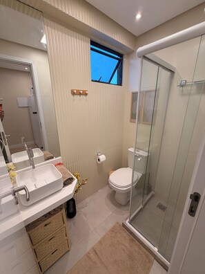 A modern bathroom with a large mirror, dual sinks, a toilet, and a glass-enclosed shower. - Paradise in Praça 19: 3 min from the village and 5 min from the natural pools! (Ipojuca)