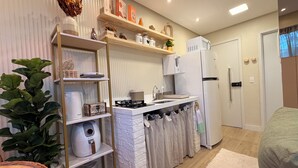 A compact kitchen with white appliances, a built-in stove, and a sink. There are shelves with decorative items and a potted plant. - Paradise in Praça 19: 3 min from the village and 5 min from the natural pools! (Ipojuca)