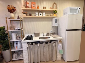 A compact kitchen with a built-in microwave, a refrigerator, a sink, and a shelf with decorative items. - Paradise in Praça 19: 3 min from the village and 5 min from the natural pools! (Ipojuca)