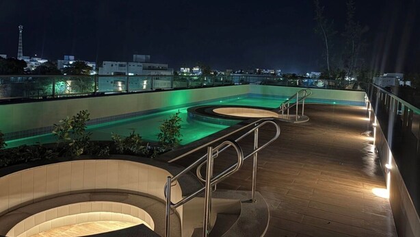 A rooftop pool area with a curved design, metal railings, and a view of the cityscape at night. - Paradise in Praça 19: 3 min from the village and 5 min from the natural pools! (Ipojuca)