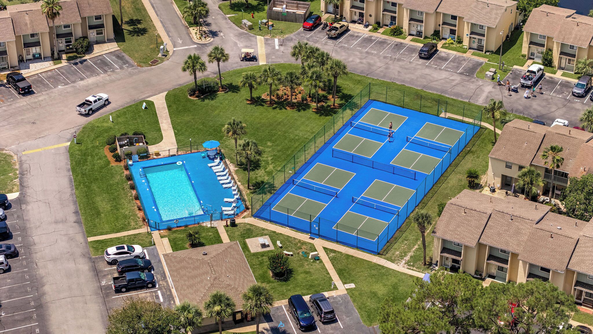 Vista aerea di una zona residenziale con piscina, campi da tennis e parcheggio.