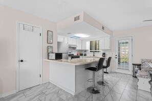 Une cuisine moderne avec des meubles blancs, un îlot central doté de tabourets de bar et un coin repas avec une table et des chaises blanches.