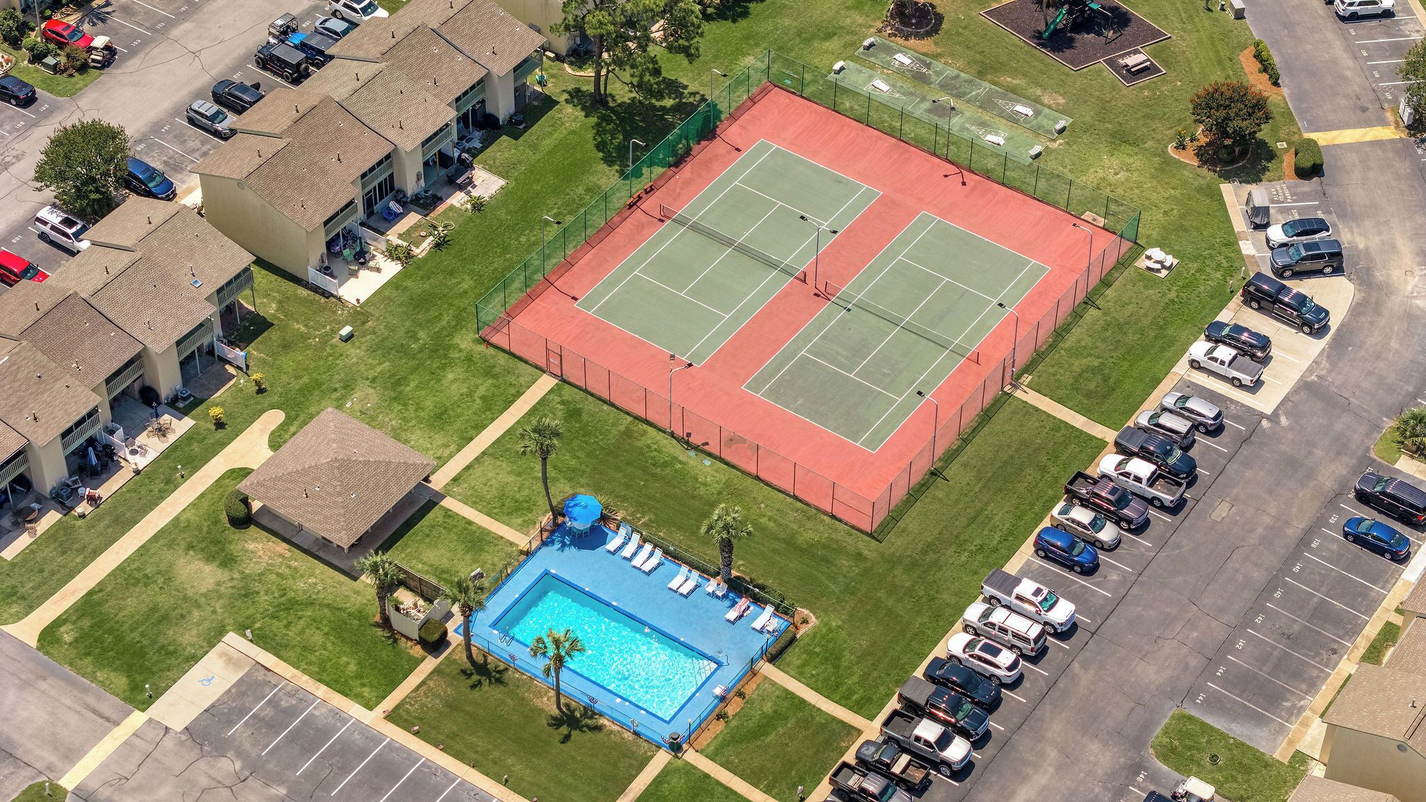 Vista aèria d'una zona residencial amb una pista de tennis, una piscina i diverses places d'aparcament.