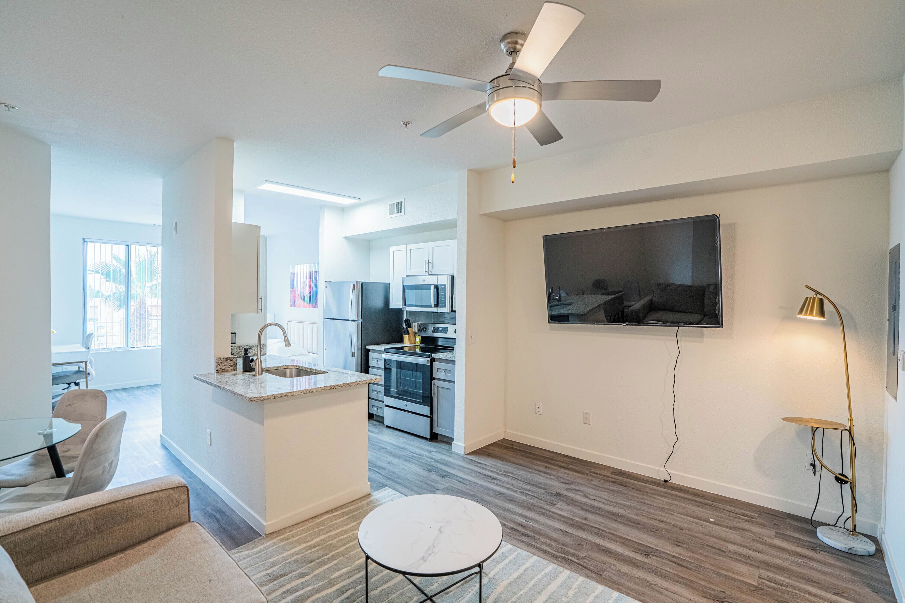 A modern living room with a ceiling fan, a TV mounted on the wall, and a small round table.