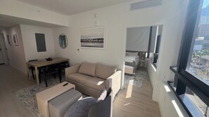 A modern living room with a sofa, a dining table, and a view of the city through large windows. - Luxury Condo 2BR/2BA Downtown Miami 905 (Miami)