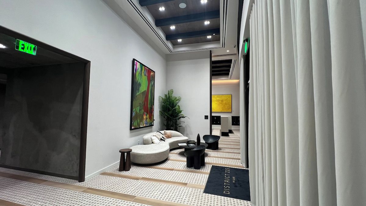 A modern lobby with a sofa, a coffee table, and a plant. There is a sign on the floor and an exit sign on the wall.