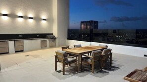 An outdoor dining area with a wooden table and chairs, a grill, and a city view at dusk. - Luxury Condo 2BR/2BA Downtown Miami 905 (Miami)