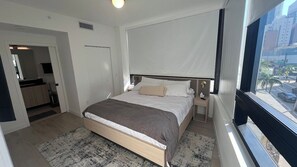 A hotel room with a bed, bedside tables, a window with a view of the city, and a door leading to another room. - Luxury Condo 2BR/2BA Downtown Miami 905 (Miami)