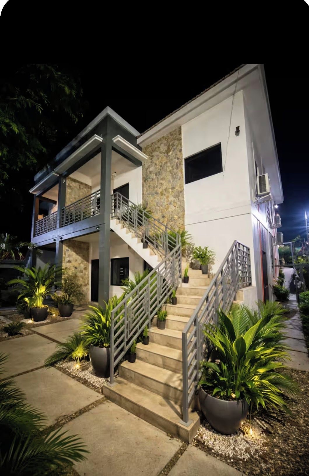 Un bâtiment moderne à deux étages, doté d’un balcon, d’un escalier et de plantes en pot.