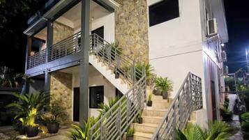 Un bâtiment moderne à deux étages, doté d’un balcon, d’un escalier et de plantes en pot.