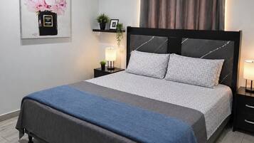 Un lit bien fait, avec une couvre-lit grise et bleue, une tête de lit noire et deux lampes de chevet.