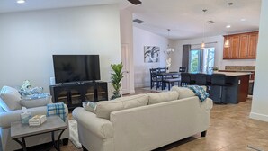 Una sala de estar moderna con un sofá color beige, un televisor de pantalla plana y una zona de comedor con una mesa y sillas.