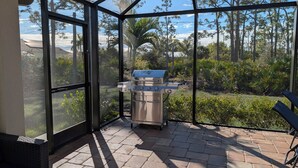 Un patio cubierto con una parrilla y zona de estar, con vistas a un jardín ajardinado y árboles.