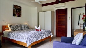 A bedroom with a bed, a ceiling fan, a wardrobe, a dining table with chairs, and a sofa.