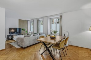 A modern living room with a sofa, TV, dining table, and chairs. - Stylish Apartment with Fast WiFi – Steps from City Center (Zürich)