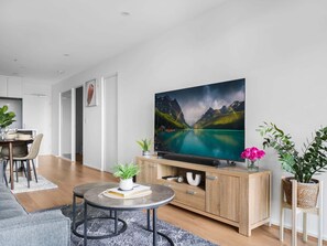 Un salon moderne doté d’un téléviseur à écran plat, d’un meuble en bois et d’un coin repas avec une table et des chaises.
