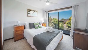 Ein Schlafzimmer mit Bett, Nachttisch, Deckenventilator, Fenster mit Blick und einem Bild an der Wand.