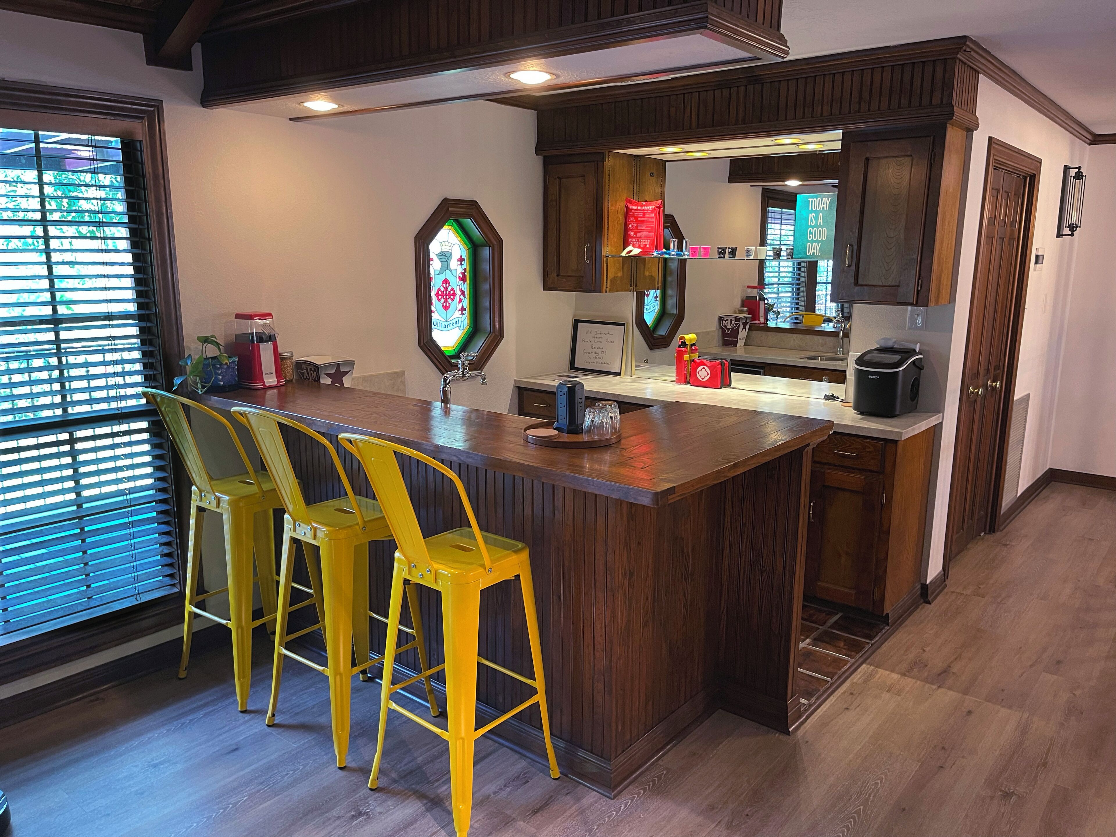 Uma cozinha com armários de madeira, um espaço de bar com cadeiras amarelas e uma janela de vitral.