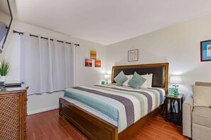 Een keurig opgemaakt slaapkamer met een bed, nachtkastjes, een stoel en een potplant.